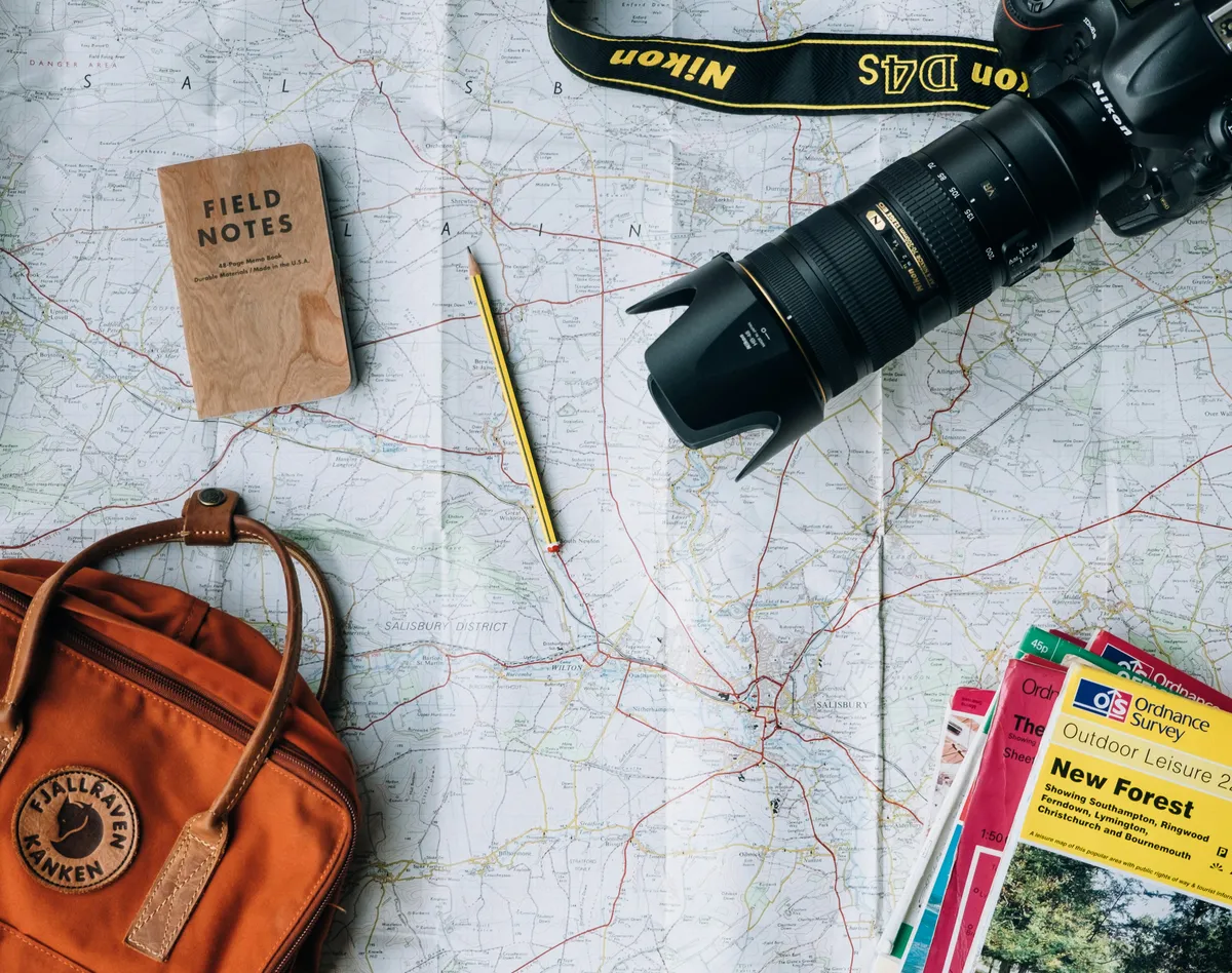 Travel planning flat lay with map, camera, notebook and backpack